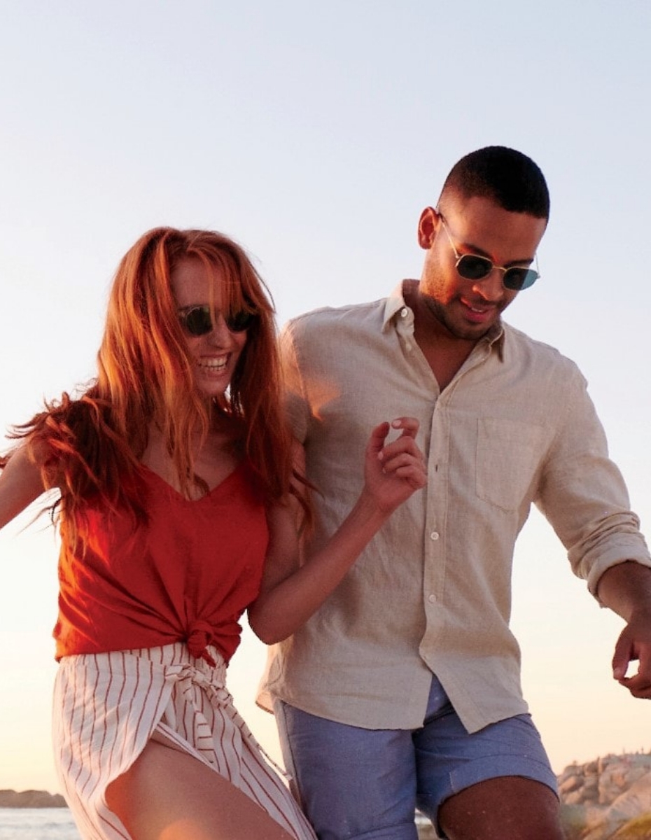 Paar geht am Strand mit Sonnenbrillen spazieren.